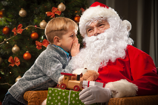 Santa Claus and a little boy. Boy tells wishes in front of Christmas Tree