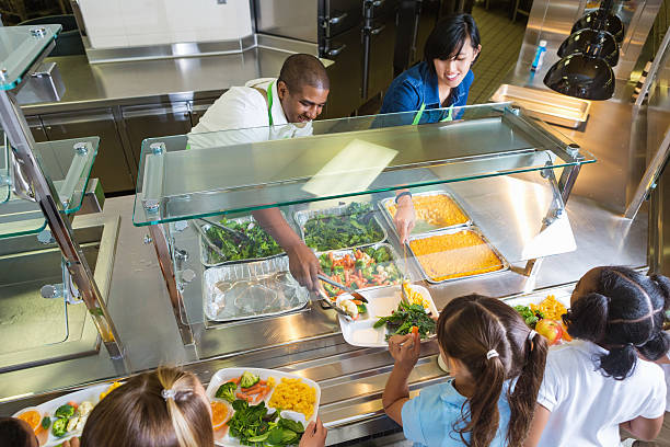 Cafeteria worker serving trays of healthy food to children Cafeteria worker serving trays of healthy food to children  cafeteria school lunch education school stock pictures, royalty-free photos & images