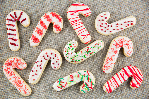 Candy cane shaped sugar cookies with frosting and sprinkles on linen cloth.
