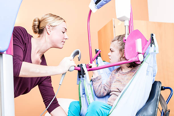 Disability a disabled child being lifted into a wheelchair Disability a disabled child being lifted into a wheelchair using a special lift and help from a nurse hoisting photos stock pictures, royalty-free photos & images