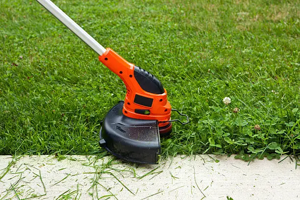 Close-up of a string weed trimmer trimming the grass along a concrete sidewalk.