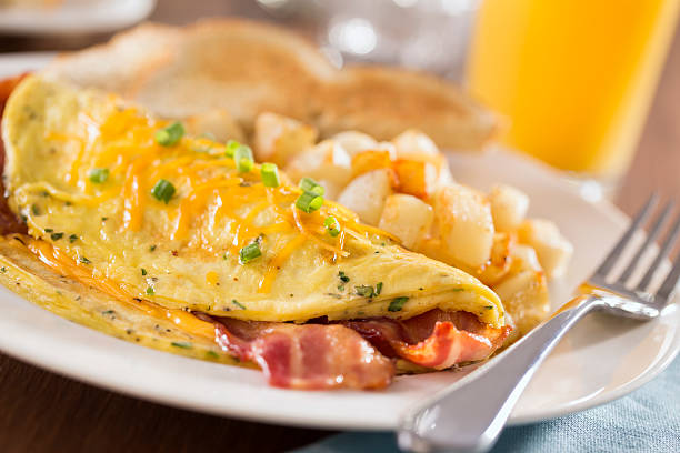 Bacon Cheddar Omelet A macro photograph of a bacon cheddar omelet with home fries (potatoes), orange juice, and toast.  The breakfast place setting  is set on a rustic wood table with a blue napkin.  Please see my portfolio for other food and drink images.  continental breakfast photos stock pictures, royalty-free photos & images
