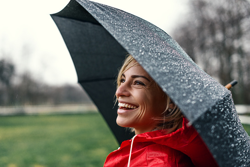 Shot of a smiling woman in red raincoat holding an umbrella.
