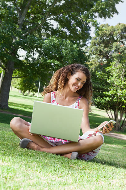 istock Pretty woman sitting in the park using laptop and texting 498553291