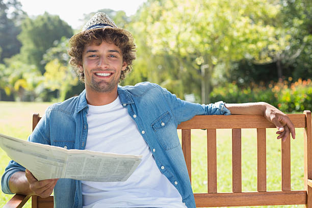 istock Hip young man sitting on park bench reading newspaper 498553367