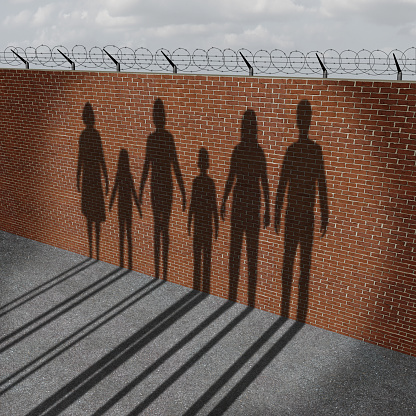 Immigration people on a border wall as a social issue about refugees or illegal immigrants crisis with the cast shadow of a group of migrating women men and children.