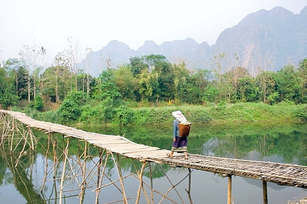 local woman walks with traditional clothes on wooden bridge. Vang Vieng, Laos - march 10, 2014: Local woman walks with traditional clothes on wooden bridge bamboo bridge stock pictures, royalty-free photos & images