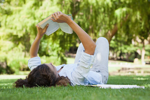istock Pretty woman relaxing on grass reading book 498556295