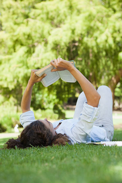 istock Pretty woman relaxing on grass reading book 498556297
