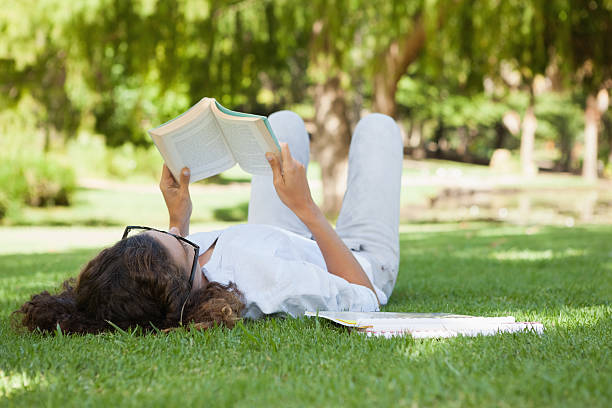istock Pretty woman relaxing on grass reading book 498556305