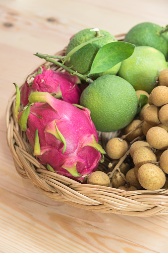 A basket consists of tropical fruits of citrus, orange, dragronfruit and longan placed on a wood background. These fruits are sweet and tasty and healthy.