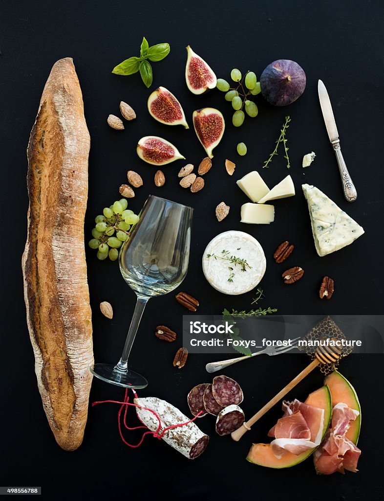 Wine and snack set. Baguette, glass of white, figs, grapes Wine and snack set. Baguette, glass of white, figs, grapes, nuts, cheese variety, meat appetizers and herbs on black grunge background, top view Wine Stock Photo