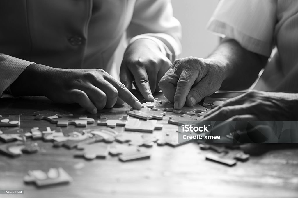 Elder care nurse playing jigsaw puzzle with senior man Elder care nurse playing jigsaw puzzle with senior man in nursing home. black and white Community Outreach Stock Photo