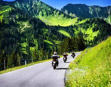 Group of travelling bikers in Alpine mountains, riding on mountainous highway, extreme lifestyle, spring travel and adventure concept