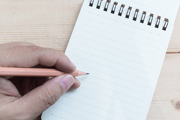 Hand hold pencile and open blank notepad on wood table