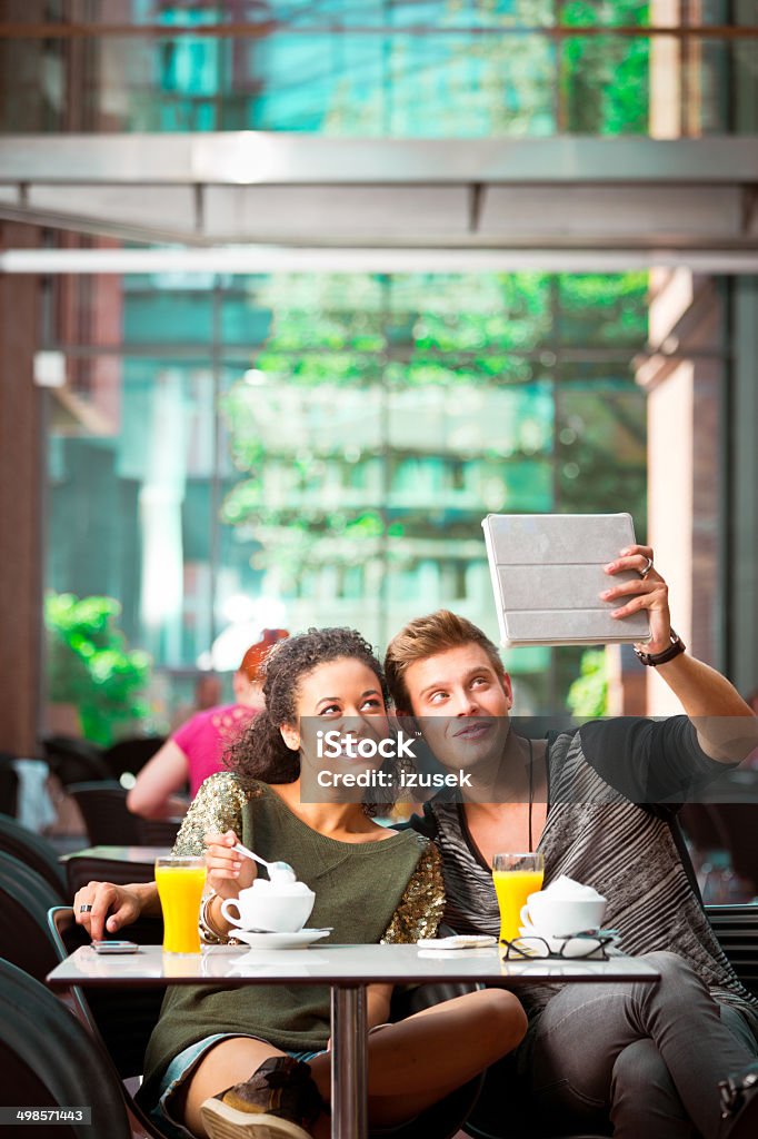 Urban young people in coffee shop Cheerful young couple sitting in cafe, photographing themselves using digital tablet. 20-24 Years Stock Photo