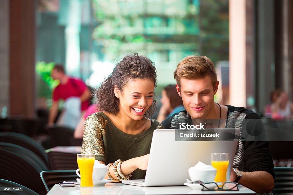 Urban young people in coffee shop Cheerful young couple sitting in cafe, using laptop together. Coffee Shop Stock Photo