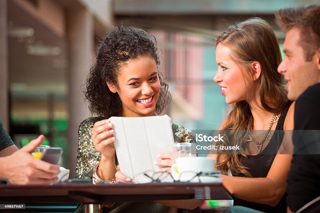 Young people using digital tablet Cheerful young urban people sitting in coffee shop and using digital tablet together. 20-24 Years Stock Photo