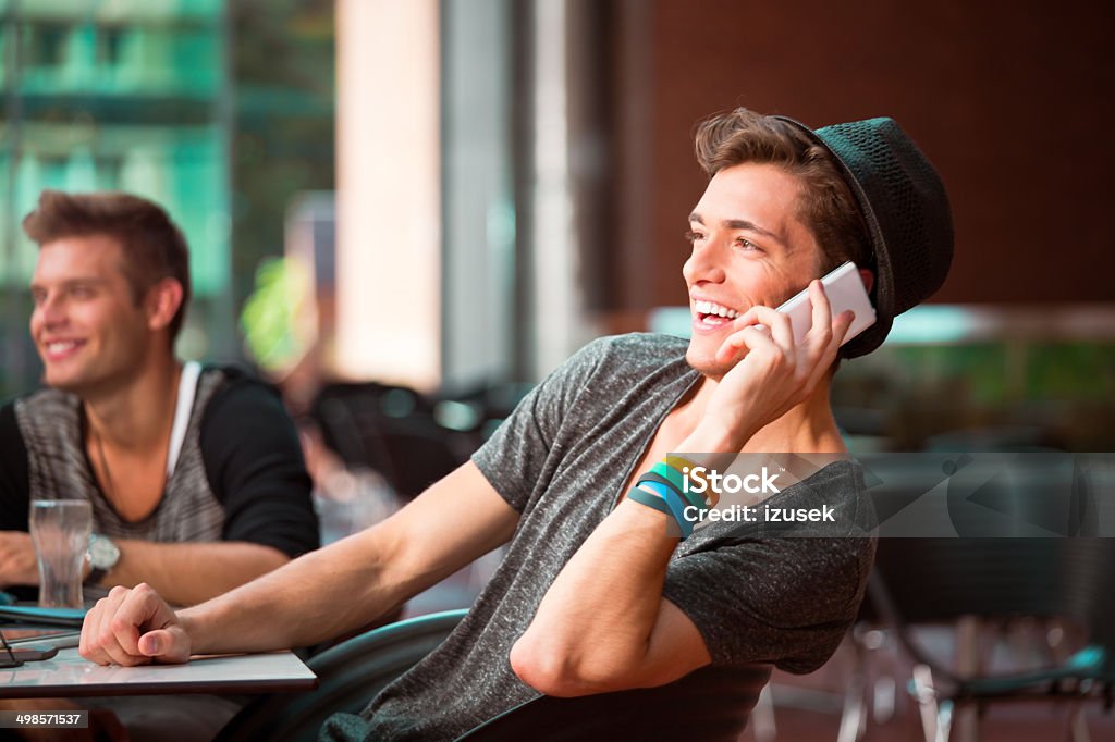 Young man on phone Cheerful young man sitting in coffee shop and talking on phone. Mobile Phone Stock Photo