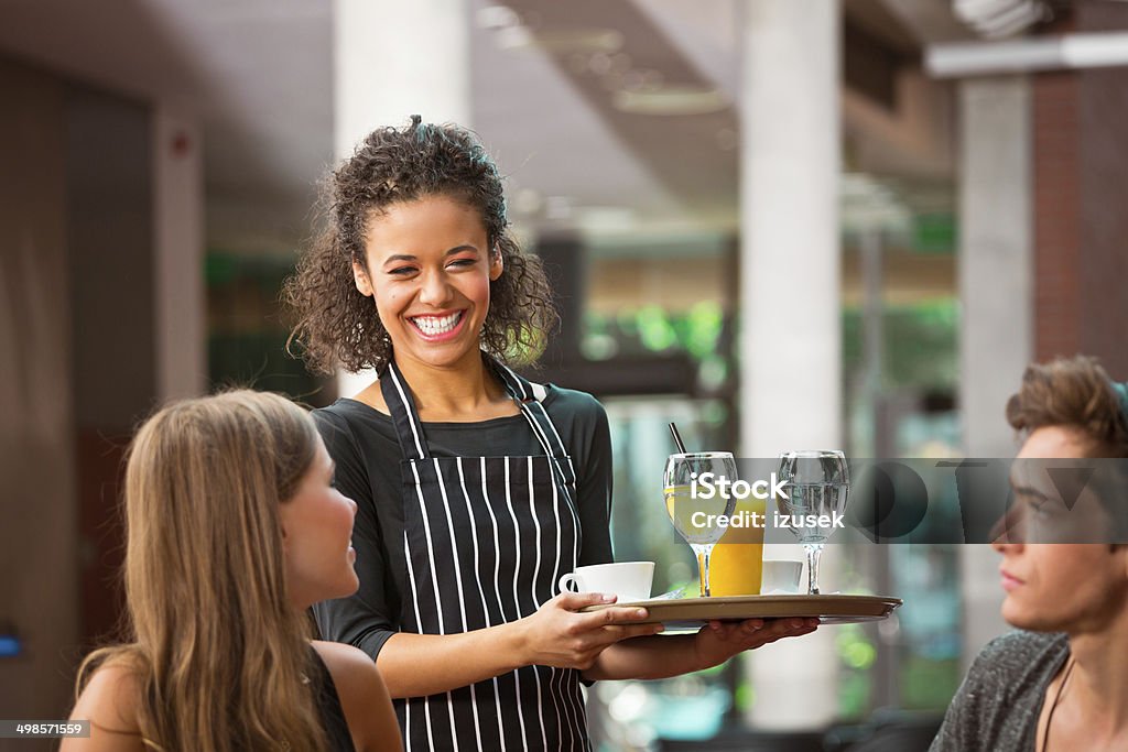 Cheerful waiter serving drinks Cheerful young female waiter serving drinks for young couple. Waiter Stock Photo