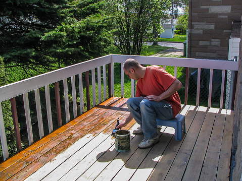 A man putting varnish on his outside wood patio deck