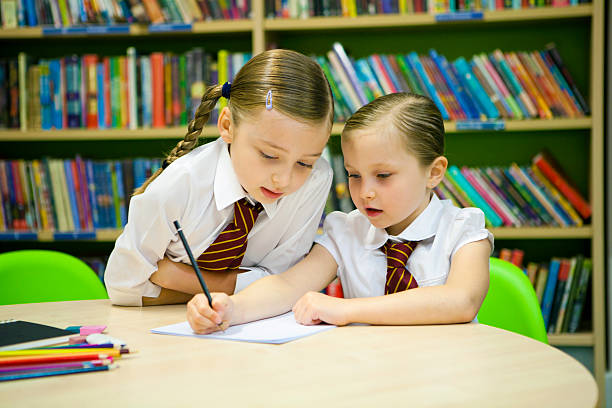 Older pupil helps this younger student with her writing stock photo