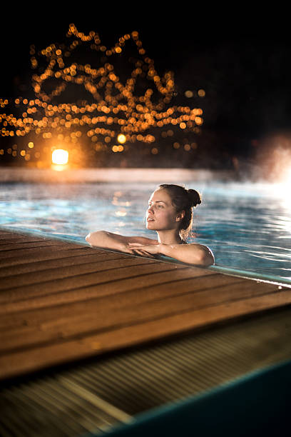 Young woman relaxing in heated swimming pool during winter night. Woman spending a winter night in a heated swimming pool. thermal pool stock pictures, royalty-free photos & images