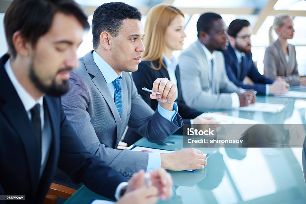 Business seminar Pensive young businessman listening to explanations at seminar surrounded by other listeners Adult Stock Photo