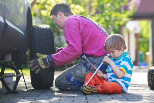 Happy family of two: father and adorable little preschool boy repairing car and changing wheel together on warm day, outdoors.