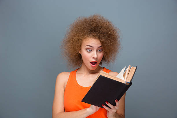 istock Wondered curly young female reading book 498602266