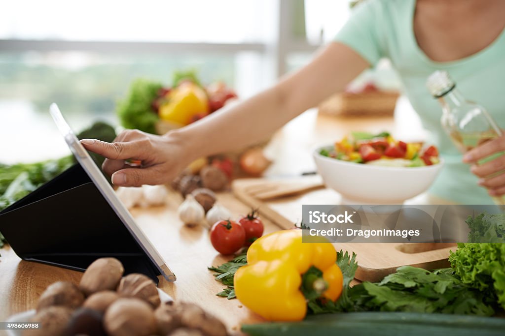 Checking recipe Woman checking recipe on digital tablet before seasoning salad Cooking Stock Photo