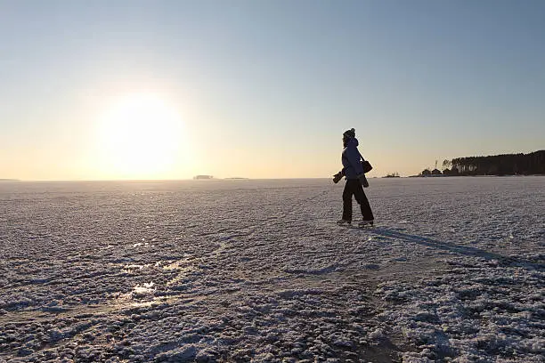 Photo of The woman skating on the frozen river at sunset
