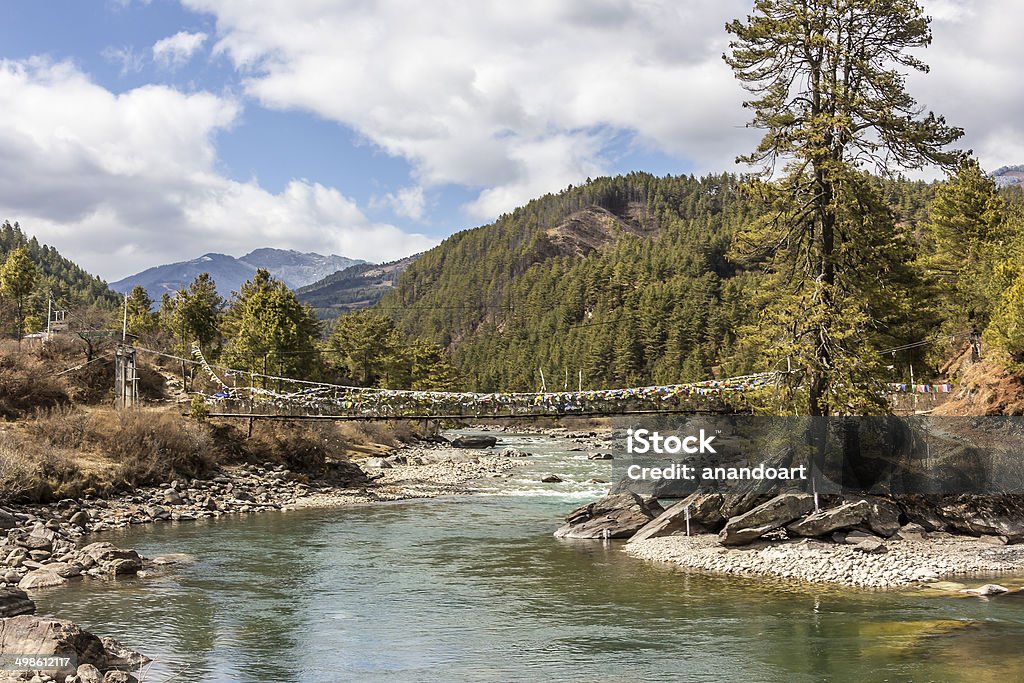 suspension bridge, Bhutan A typical bhutanese suspension bridge leading over a creek or small river in Bhutan. The bridge is covered with prayer flags, In the background are the mountains. Bumthang Stock Photo