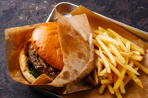 Burger with meat and French fries in aluminum tray on dark background