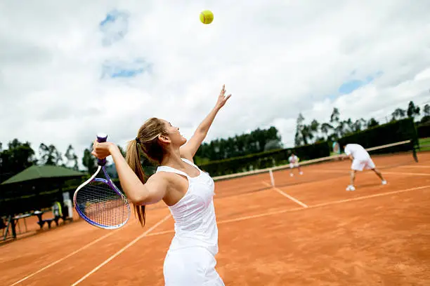 Woman playing doubles at tennis and serving