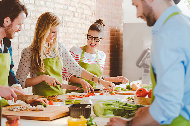 Four people taking part in cooking class Group of people wearing aprons taking part in cooking class, preparing food, slicing vegetables, talking, laughing. cooking class photos stock pictures, royalty-free photos & images
