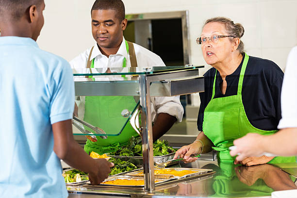 High school cafeteria lunchroom workers serving hot meal to students High school cafeteria lunchroom workers serving hot meal to students cafeteria worker photos stock pictures, royalty-free photos & images