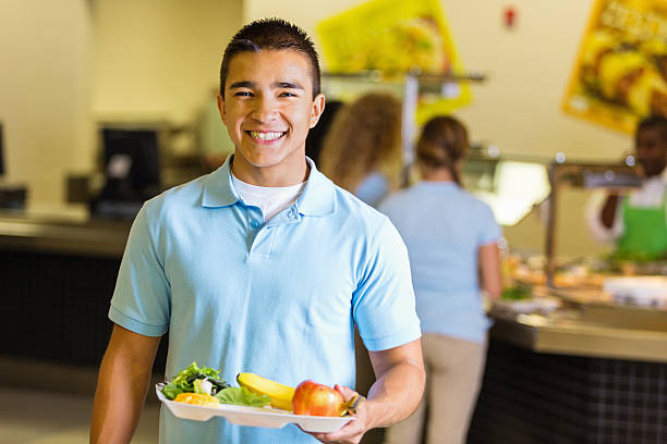 Happy student holding tray of healthy food in school lunchroom Happy student holding tray of healthy food in school lunchroom school lunch child food lunch stock pictures, royalty-free photos & images