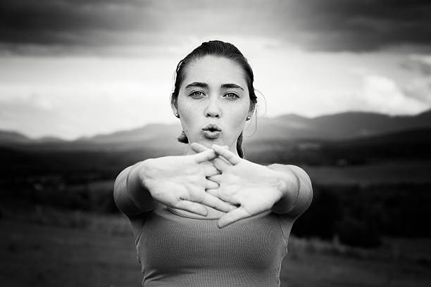 Young athlete stretching her arms outdoors while exhaling. Black and white image with a slight sepia tone.