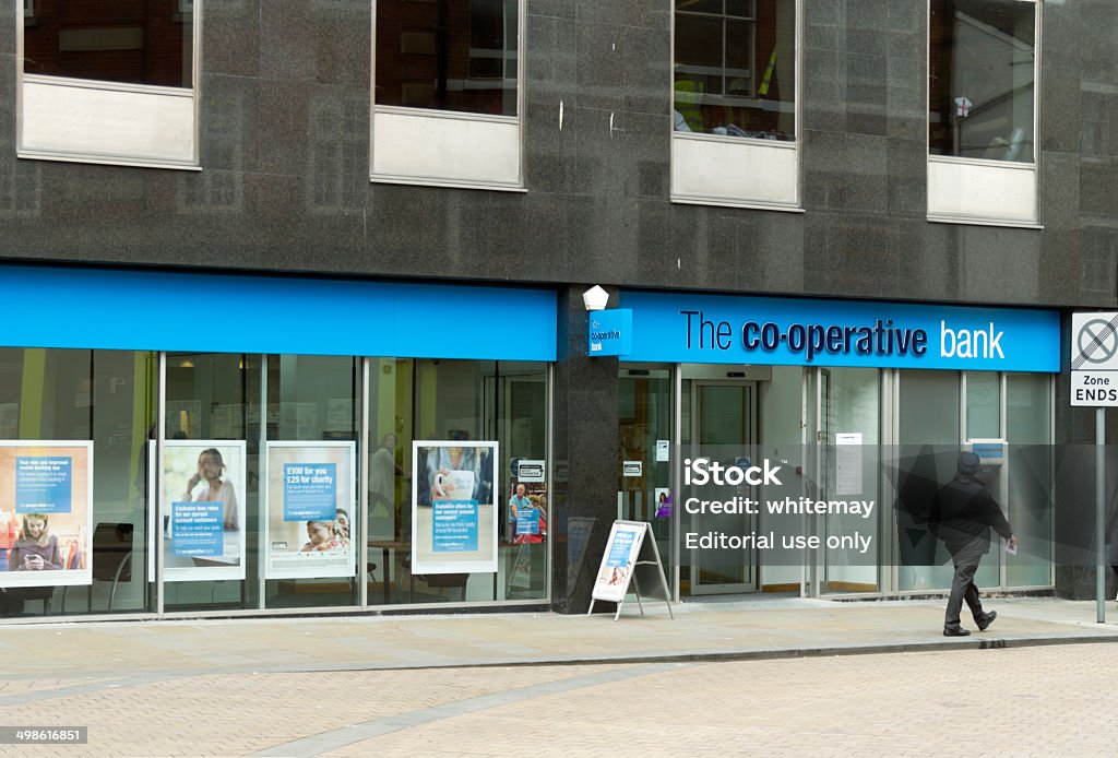 Co-operative Bank branch in Ipswich Ipswich, Suffolk, England - June 16, 2014: A man passing a branch of the Co-operative Bank in Ipswich, Suffolk, in Eastern England. The Co-operative Banking Group, a British commercial bank, is part of the Co-operative Group, the largest co-operative in the country, and was formed in 1872 as the Loan and Deposit Department of the Manchester Co-operative Wholesale Society: it became the CWS Bank a few years later. (Dull day. Motion blur on man.) Bank - Financial Building Stock Photo