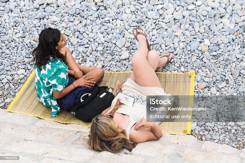 Doodling on the Beach Nice, France - June 4, 2014: A girl doodles in a small notebook with a pen while relaxing with a friend on a straw mat against the seawall on the French Riviera Adult Stock Photo