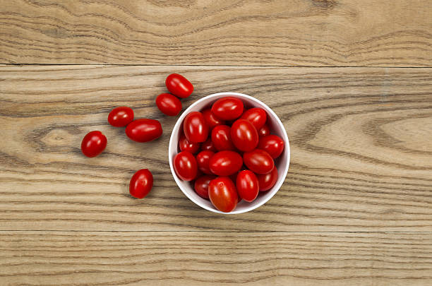 Fresh Grape Tomatoes in Bowl on Aged Wood Overhead view of fresh grape tomatoes in white bowl placed on rustic wooden boards. grape tomato stock pictures, royalty-free photos & images