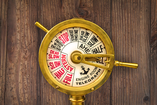 Vintage nineteenth century engine room telegraph in front of an old wooden wall