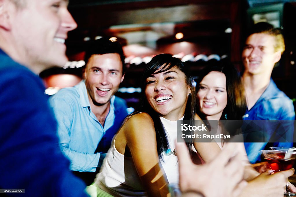 Happy interaction between friends at club bar Five smiling friends share a joke as they sit at the bar on a fun night out. 20-29 Years Stock Photo