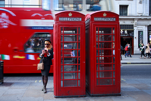 London, UK - April 28, 2014: A black woman with coloured hair using a mobile phone while standing next to the famous red telephone booth in London near Trafalgar Square.