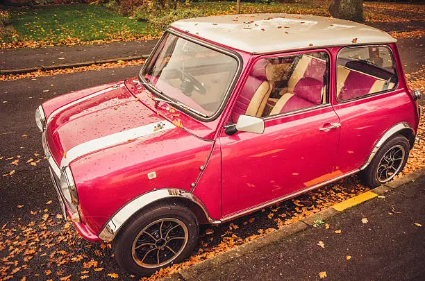 Classic mini car in pink colour parked at the street in Autumn.