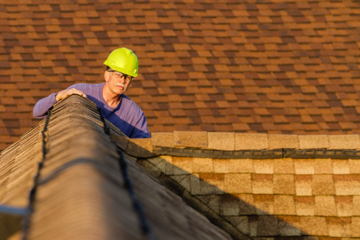 An inspector looks over a residential roof at the peak.