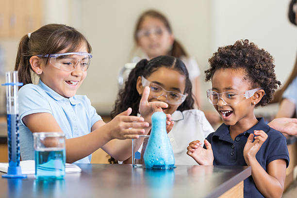 excited girls using chemistry set together in elementary science classroom - basisschool stockfoto's en -beelden