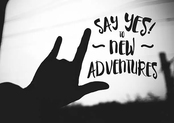 Inspiration quote : "Say yes to new adventures" on silhouette Hand love sign on road ,Motivational typographic.