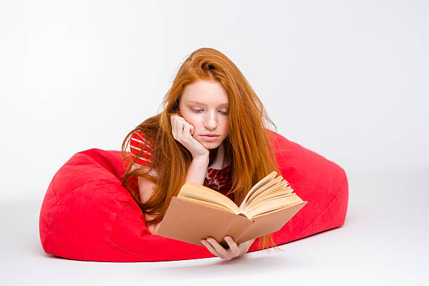 istock Concentrated girl relaxing in red bean bag and reading book 498659412